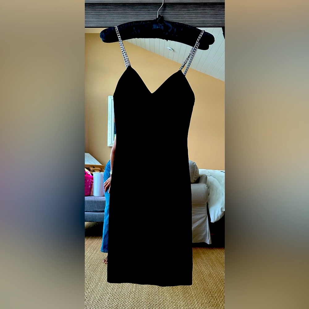Classic black stretchable fabric cocktail dress with gold shoulder chain.